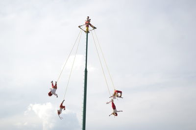 Low angle view of people hanging on ropes against sky