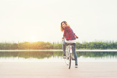 Woman riding bicycle on pier over lake against sky