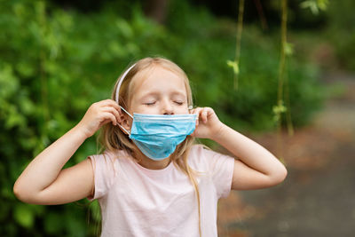 Happy little girl takes off protective medical mask from face outdoors. victory over coronavirus