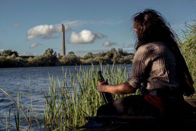 Rear view of woman sitting by lake against sky