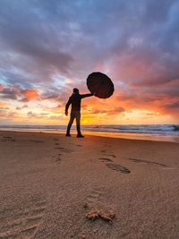 Rear view of woman standing at beach against sky during sunset