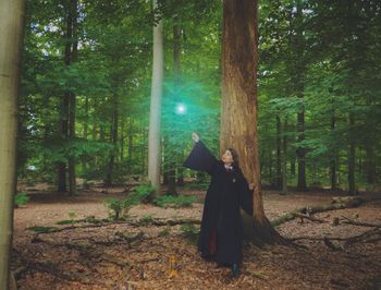 Woman standing by tree trunk in forest