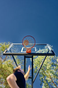 Low angle view of man putting ball in basketball hoop against clear sky