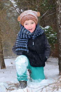 Full length portrait of boy kneeling on snow covered field