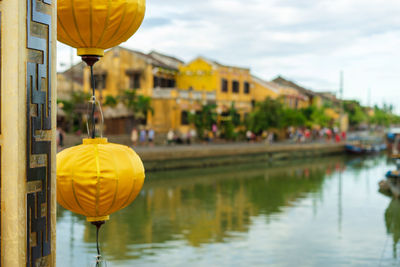 Close-up of yellow balloons on lake by buildings against sky