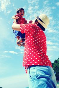 Low angle view of father lifting crying son against sky during sunny day