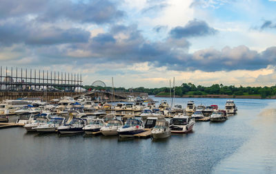 Boats in harbor against cloudy sky