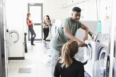 University student talking to woman by washing machine while friends standing in background