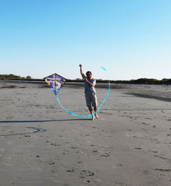 Man flying kite while standing on sand at beach against clear sky
