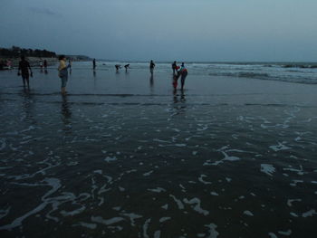 People on wet beach against sky