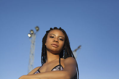 Low angle view of young woman with arms raised against blue sky