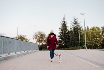 Woman with dog walking on walkway against sky