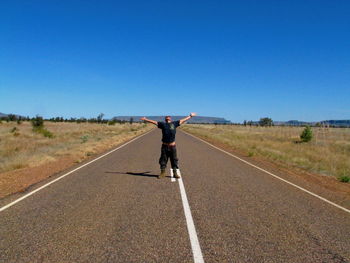 Rear view of man on road against clear blue sky
