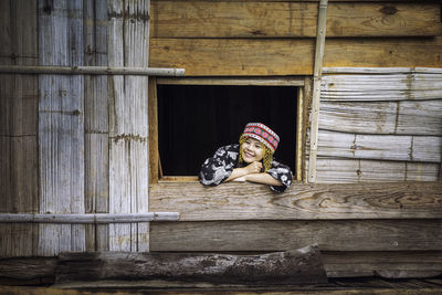 Smiling woman peeking through window of wooden house