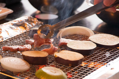 Cropped hand roasting meat and vegetables on barbecue