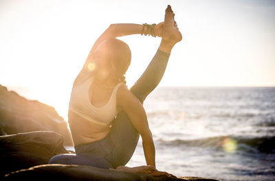 Woman sitting by sea against clear sky