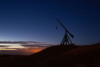 Silhouette windmill on land against sky at night