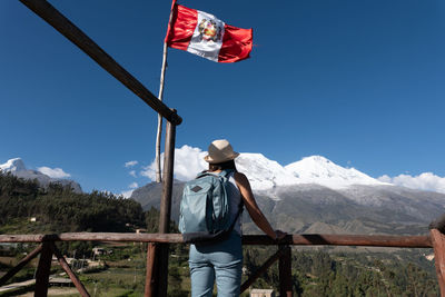 Tourist at a viewpoint with a peruvian flag observes the mountain named huascaran.