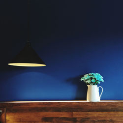 Illuminated pendant light over table against wall