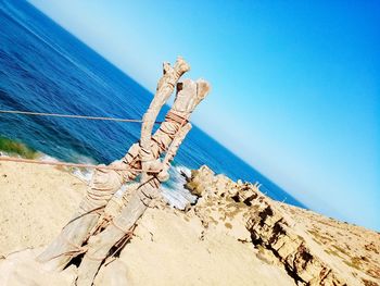 Tilt image of driftwood on beach against clear blue sky