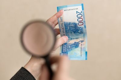 Cropped hand holding paper currency and magnifying glass