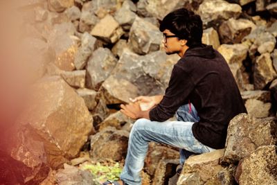 Side view of young man sitting on rock