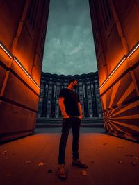 Rear view of man standing by building against sky during sunset