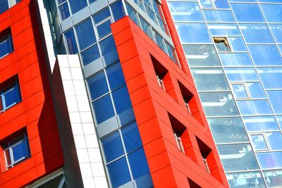 Part of the facade of a modern building with red walls, square windows, the blue mirrored glass. 