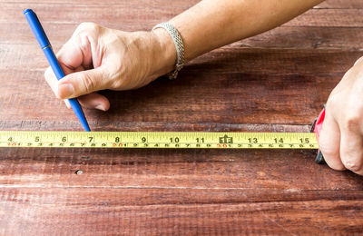 Close-up of hand measuring wooden table with tape