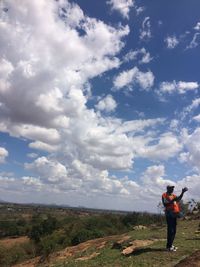 Rear view of woman standing on field against cloudy sky