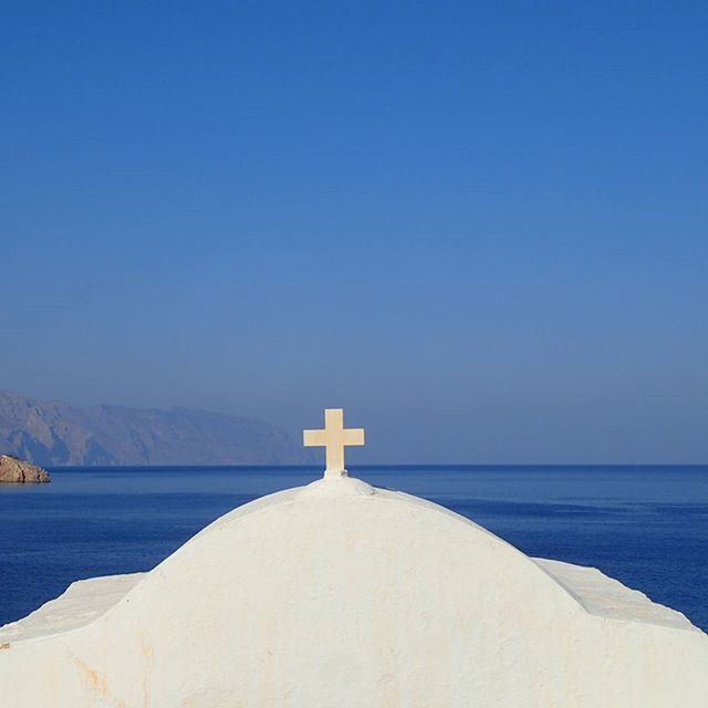 sea, clear sky, copy space, water, blue, tranquil scene, scenics, tranquility, beauty in nature, nature, mountain, horizon over water, built structure, idyllic, lighthouse, outdoors, architecture, mountain range, day, remote