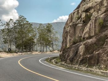 Road by trees and mountains against sky