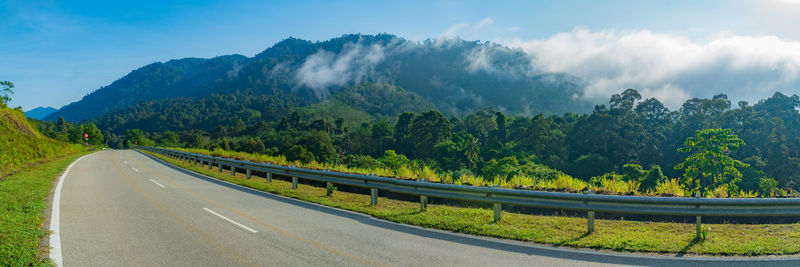 Country road amidst trees against sky