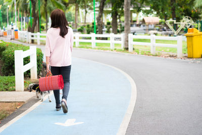 Rear view of woman with dog walking on road in city