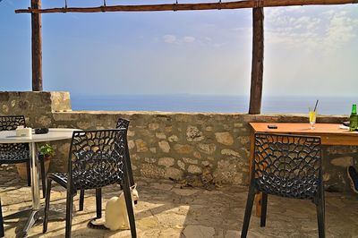 Empty chairs and table by sea against sky