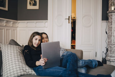 Smiling girls using laptop while resting on sofa at home