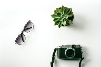 High angle view of camera with plant and sunglasses on white background