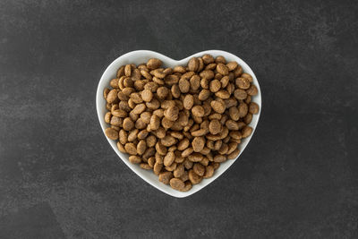 Appetizing dry cat food in a heart-shaped bowl on a dark background.