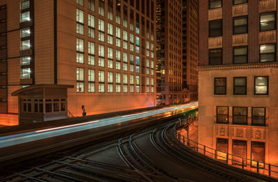 Railroad tracks amidst buildings in city at night