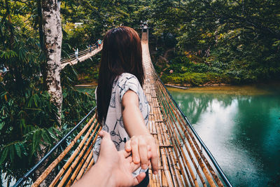 Low section of woman sitting on footbridge over lake