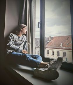 Girl looking away while sitting on window sill at home