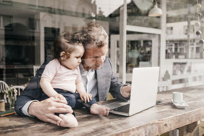 Businessman with little daughter working on laptop in cafe