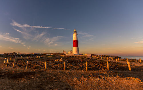 Lighthouse by sea against sky during sunset