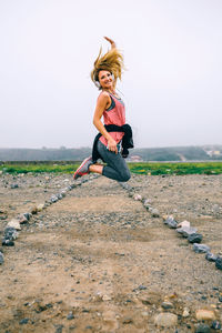 Portrait of young woman with arms outstretched against clear sky