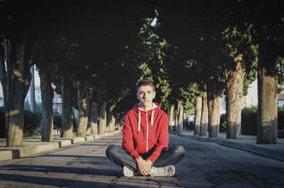 Portrait of young man sitting on street amidst trees