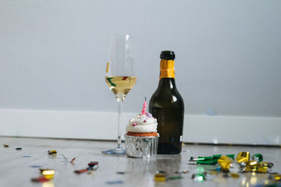 Bottle and glass of champagne and cupcake with candle on floor with confetti after birthday party