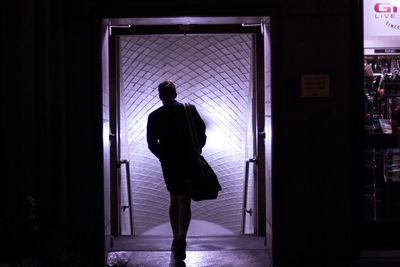 Rear view of silhouette man standing against door at night