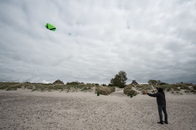 Rear view of man flying kite at beach against cloudy sky