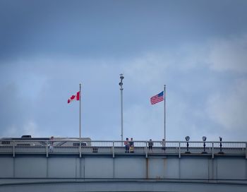 Low angle view of two flags in canadian usa border against sky in city