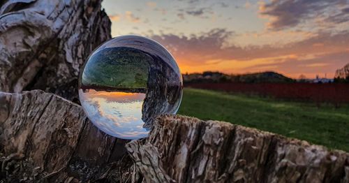 Close-up of crystal ball on landscape against sky at sunset